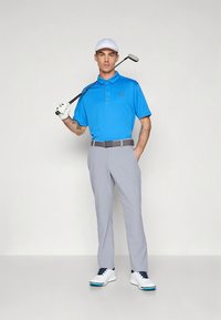 Vyrų golfo apranga, kurią sudaro mėlynas polo marškinėlis, pilkos kelnės ir balti batai. Išskirtiniai bruožai – tvarkingas dizainas ir golfo klubo priedas.