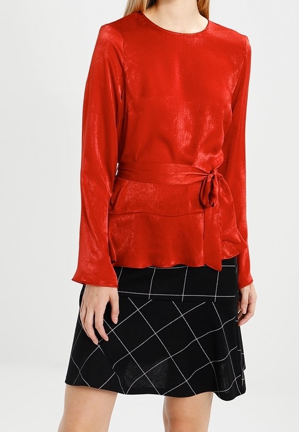 Top lungo a maniche con una cintura in vita di raso rosso, abbinato a una gonna nera con un motivo a griglia bianca. Tessuto liscio e design aderente.