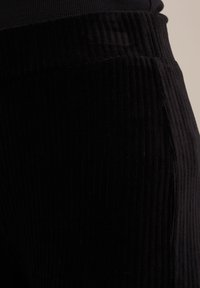 Detailní záběr na černou žebrovanou tkaninu, která se vyznačuje měkkou strukturou a vertikálními vzory; pas je široký a elastický pro pohodlí.
