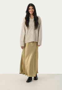 Beige knitted sweater with diamond patterns, paired with a long golden satin skirt and black ankle boots, standing against a white background.
