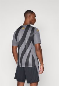 Grå sportsdrakt med svarte striper, korte ermer, og Kappa-logo i gull på skuldrene. Kombinert med svarte shorts. Glatt tekstur.