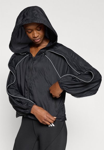 Μαύρο ελαφρύ μπουφάν με κουκούλα, διαθέτει φερμουάρ μπροστά, ελαστικά τελειώματα στα μανίκια και αντίθετη γκρι λεπτομέρεια κατά μήκος των ραφών.