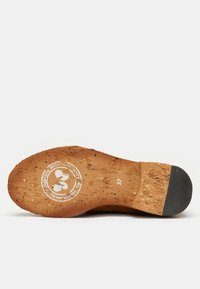 Suela de corcho con superficie texturizada y tacón de goma negra. El logotipo en relieve presenta un diseño circular con el texto "HECHO CON AMOR DESDE." Se indica la talla 37.