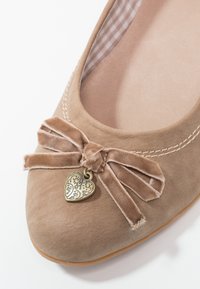 Chaussure plate en daim beige avec un bout arrondi, un nœud en satin orné d'un charm en forme de cœur, et une doublure en tissu à carreaux. Texture lisse avec des détails cousus.