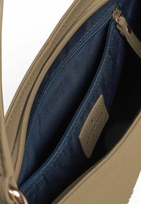 Beige Lederhandtasche Innenraum mit blauer Stoffauskleidung, Reißverschlussfach und einem strukturierten Etikett mit Markenname.