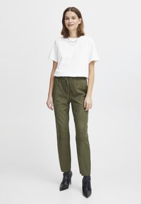 Hvit kortermet t-skjorte kombinert med grønne faux suede joggebukser med elastisk midje og sidelommer, komplementert av sorte ankelstøvletter.