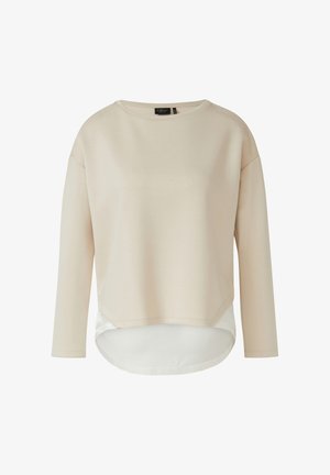 Beżowa warstwowa damska bluzka z długim rękawem, okrągłym dekoltem i białym, wydłużonym dołem z tyłu, widoczna metka marki wewnątrz kołnierzyka.