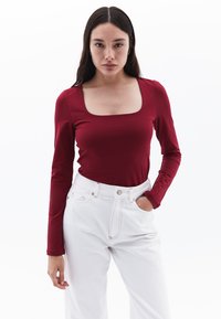 Langarm, top met vierkante hals in bordeauxkleurige stof, gecombineerd met hoge witte jeans. Soepele textuur, getailleerd ontwerp.