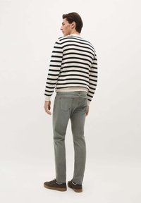 Gestickter Pullover mit navy und cremefarbenen horizontalen Streifen, runder Ausschnitt; kombiniert mit hellgrauen Hosen und braunen Schuhen, von hinten betrachtet.