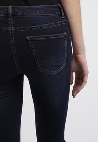 Mörkblå denimjeans med slim fit, som har bakfickor och kontrasterande sömmar. Slät textur, hög midja, minimala design detaljer.