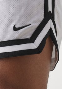 Calções de basquetebol Nike em malha branca, com riscas laterais pretas e um logótipo preto. Abertura arredondada com tecido texturizado e detalhes de costura.