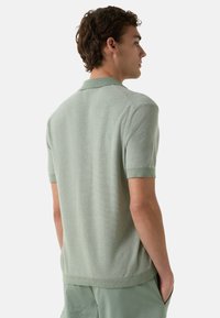 Kortærmet, strikket polo-shirt i lysegrøn. Har en tekstureret finish, ribbet krave og manchetter, samt en tætsiddende silhuet.