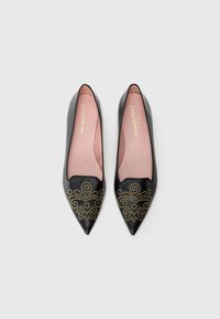 Ballerines noires à bout pointu en cuir ; motif floral décoratif en studs dorés à l'avant ; semelle intérieure rose pâle visible à l'intérieur.