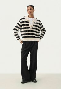 Pull en tricot à rayures noires et blanches avec un large col, doté d'une coupe ample et de poignets côtelés, associé à un pantalon large noir.