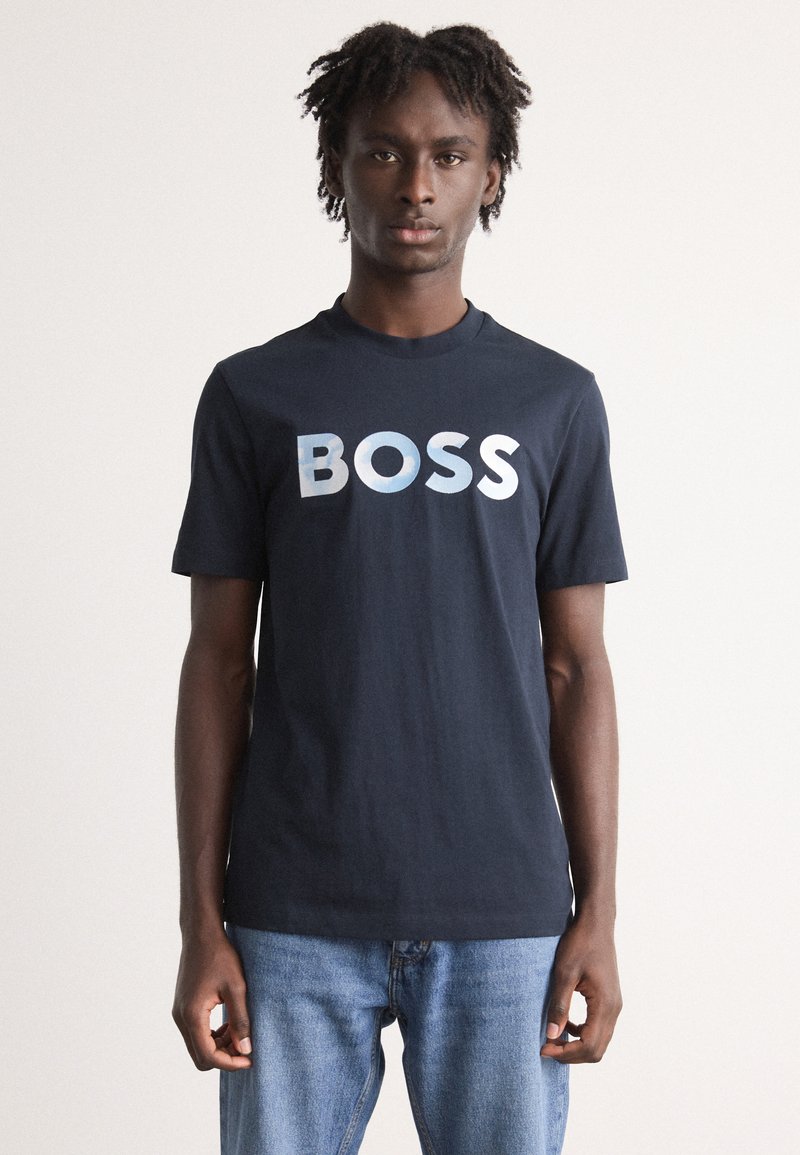 Tamsiai mėlynas medvilninis marškinėlis, turintis didelį, šviesiai mėlyną gradientinį "BOSS" logotipą per krūtinę, su trumpomis rankovėmis ir apvaliu iškirpimu.