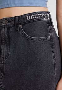 Jeans in denim neri con vita alta, dotati di una tasca frontale e del nome del brand ricamato in bianco sulla cintura. Texture liscia.