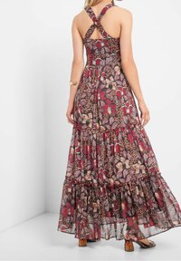 Maxiklänning med ett blommönster i rött, brunt och teal. Volangkant, korskorsade axelremmar och en nyckelhålssydd bakdetalj förstärker designen.