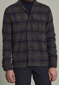 Brun och marinblå rutmönstrad skjortjacka med en borstad textur, knäppning fram och en bröstficka. Långa ärmar med manschettknappar.