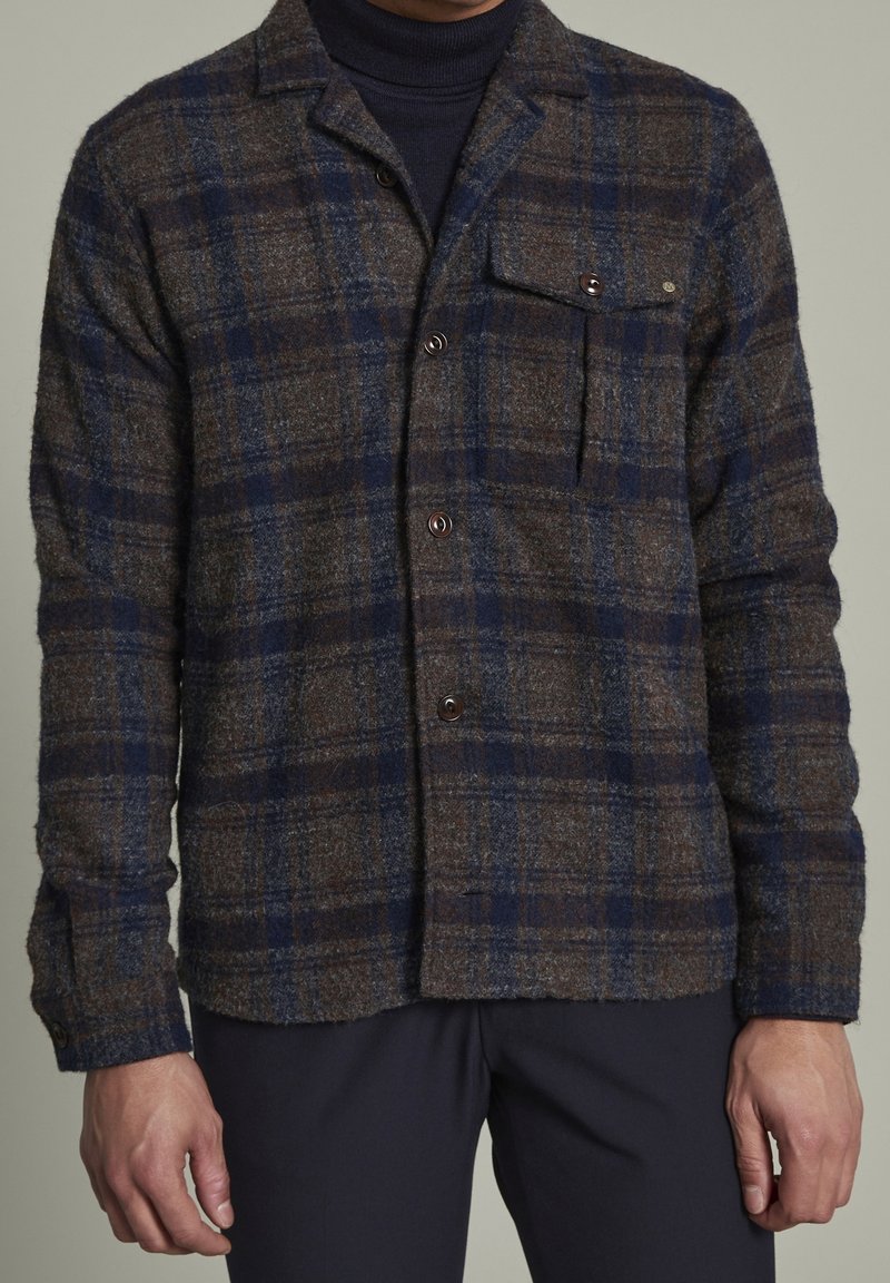 Brun och marinblå rutmönstrad skjortjacka med en borstad textur, knäppning fram och en bröstficka. Långa ärmar med manschettknappar.