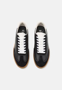 Black sneakers with white laces and stitching; suede and leather materials; gum outsole; minimalist design; padded collar; logo on insole.