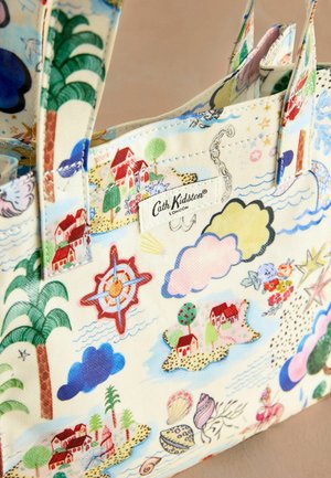 Bolso de tela con un diseño colorido y náutico que presenta casas, nubes, árboles y una brújula. Etiqueta de la marca visible.