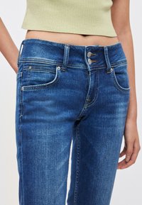 Jeans hlače iz srednje prane bombažne tkanine z oprijetim krojem, ki imajo dva sprednja žepa, zadrgo z gumbi in subtilne bledenje.