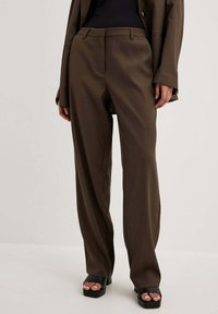 Brązowe, dopasowane spodnie z prostymi nogawkami, subtelnym połyskiem, kieszeniami z przodu i szlufkami na pasek, w zestawie z czarnymi sandałami na platformie.
