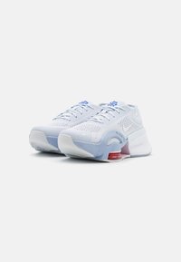 Zapatillas deportivas blancas con parte superior de malla transpirable, acentos en azul claro, suela acolchada y detalles rojos en el talón.