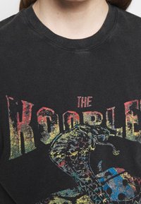 Camiseta negra de algodón con un gráfico colorido y desgastado de una serpiente y el texto "THE KOOBLE" en letras grandes y desgastadas.