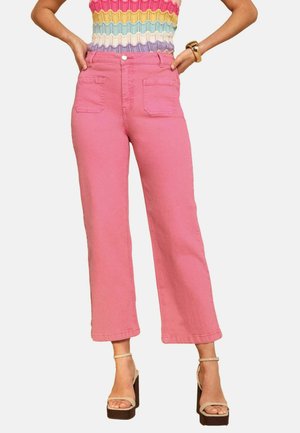 Naine, kes kannab roosakaid kõrge vöökohaga lühikesi teksapükse, mitmevärvilist triibulist kootud topi ja beežide platvormsandaale pahkluudega rihmadega.