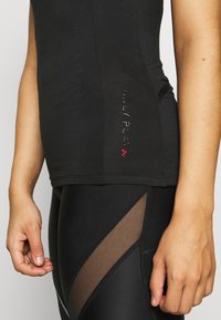 Camiseta atlética negra de diseño ajustado. Presenta un logo brillante "ONLY PLAY" en el lateral. Combinada con leggings negros con detalles de malla.