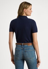 Μπλε ναυτικό πόλο μπλουζάκι με κοντά μανίκια και κλασικό γιακά. Φορεμένο με ψηλόμεσο μπλε τζιν και καφέ δερμάτινη ζώνη.