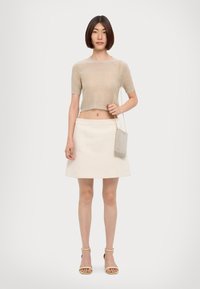 Haut en tricot cropped beige à manches courtes, associé à une jupe A-line crème. Elle tient un sac mini métallisé et porte des sandales à brides beiges.