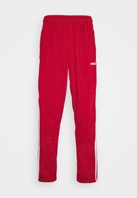 Czerwone spodenki sportowe wykonane z poliestru, z elastycznym paskiem w talii, białymi paskami po bokach i białym logo Adidas z przodu.