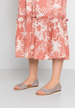Bas des jambes portant des ballerines ouvertes en daim taupe associées à une jupe midi à motif floral corail et blanc avec un détail volanté.