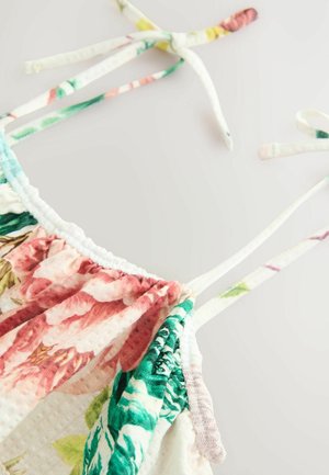 Camisole à motif floral avec bords festonnés, aux couleurs pastel comme le rose et le vert. Bretelles réglables à nouer, fabriquée en tissu léger.
