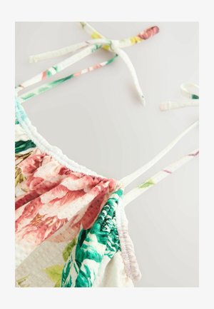 Camisole a fantasia floreale con orli arricciati, caratterizzata da colori pastello come il rosa e il verde. Spalline regolabili con nodo, realizzata in tessuto leggero.