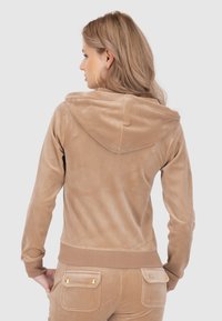 Hoodie in velluto marrone chiaro con cappuccio regolabile, polsini aderenti e vita a costine. Texture liscia e design minimalista.