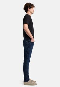Svart crew-neck t-shirt, mörkblå jeans och beige sneakers. Slim fit jeans med minimal sömnad och sidofickor. Lockigt hår.