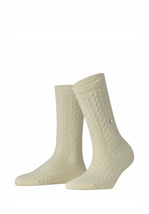 Par de calcetines de punto texturizado color crema hasta la mitad de la pantorrilla, con un sutil patrón de trenzas y un pequeño logo metálico redondo en el lateral.