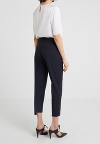 Granatowe spodnie o dopasowanym kroju, skrócone i z bocznymi rozcięciami. Połączone z białą bluzką z tylnym otworem w kształcie klucza i krótkimi rękawami.