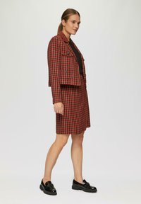 Czerwono-czarny zestaw żakietu i spódnicy w wzór houndstooth; strukturalny design z krótkim żakietem, który ma klapy i podwójne guziki.