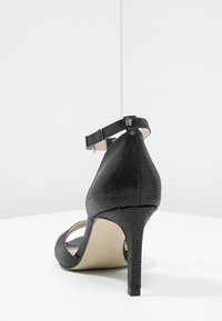 Black high-heeled sandal with textured faux snake skin, ankle strap, open toe, and a slender stiletto heel. Interior is a contrasting light color.