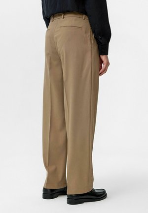 Brown wide-leg pants with a smooth texture, featuring a single back pocket and a crease down the front, worn with black shoes.