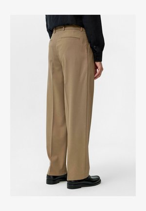 Brown wide-leg pants with a smooth texture, featuring a single back pocket and a crease down the front, worn with black shoes.