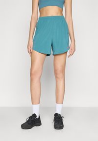Shorts atléticos em verde-água com um cós elástico e logo rosa. Usados com sapatos de caminhada pretos e meias brancas, exibindo um ajuste descontraído.