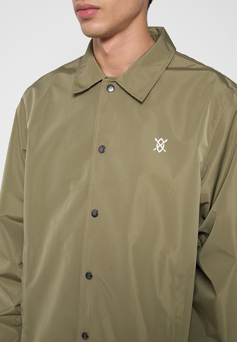 Olijf groen lichtgewicht jasje met een kraag, drukknoopsluiting en een klein wit logo aan de linkerkant. Gladde, glanzende stof.