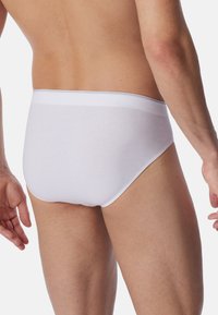Weiße Baumwollunterhosen mit glatter Textur, elastischem Bund und klassischem Schnitt, von hinten auf einem neutralen Hintergrund gezeigt.