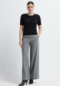 Haut noir à manches courtes avec un col texturé et un pantalon large gris, arborant un léger motif à carreaux et des escarpins noirs à bout pointu.