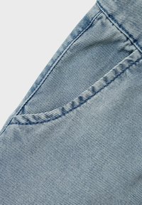 Tela de mezclilla azul claro que muestra un primer plano de una costura y los detalles del bolsillo, con sutiles rayas verticales y costuras en contraste.